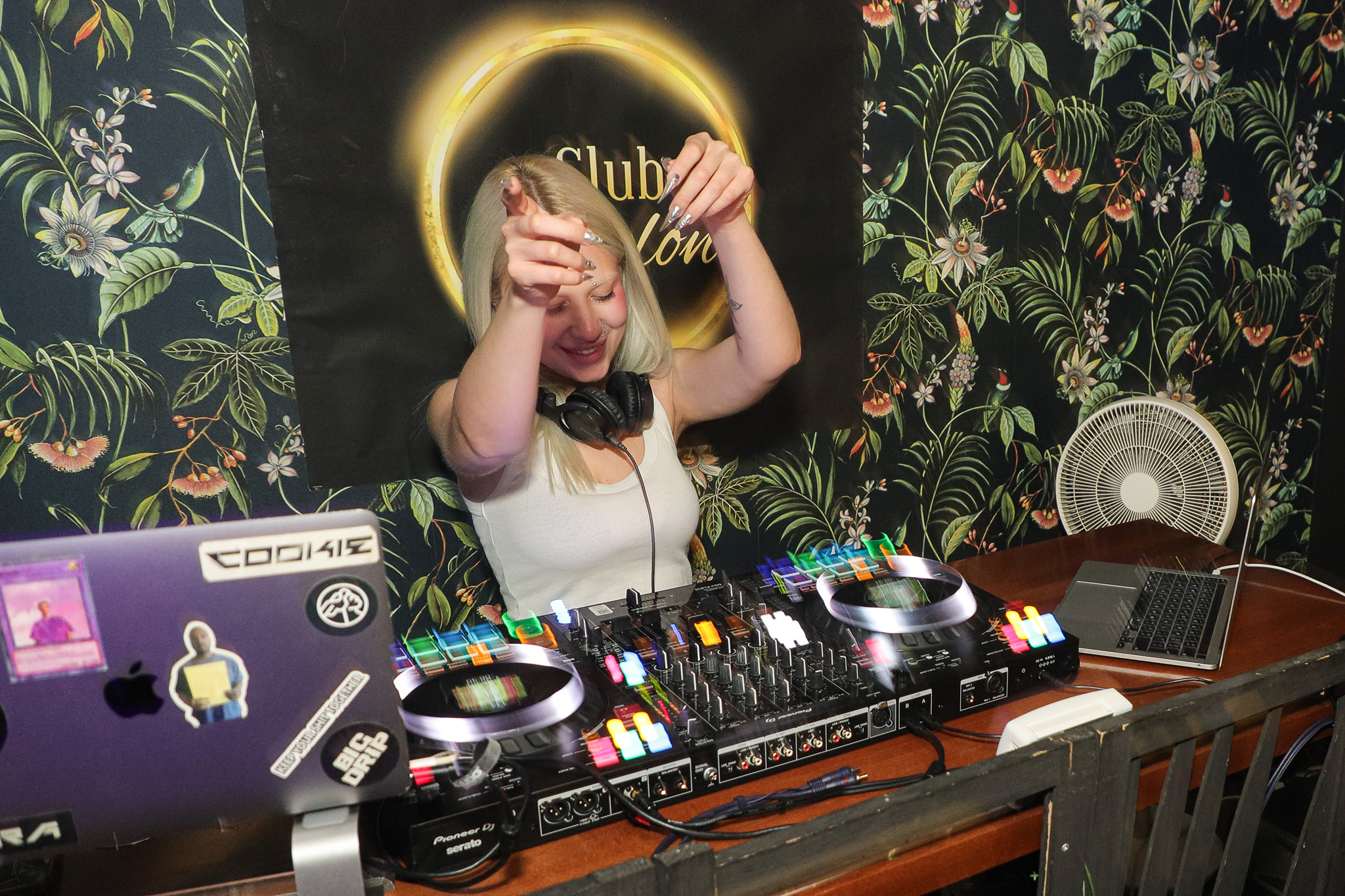 A DJ smiling and pointing at the crowd from behind the decks.