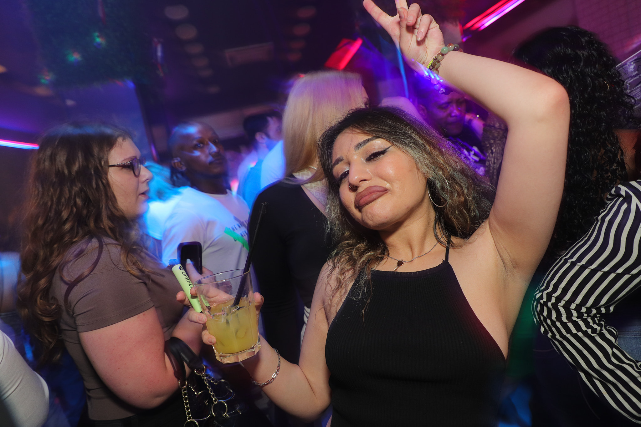 A woman holding a drink and making a peace sign on the dance floor.
